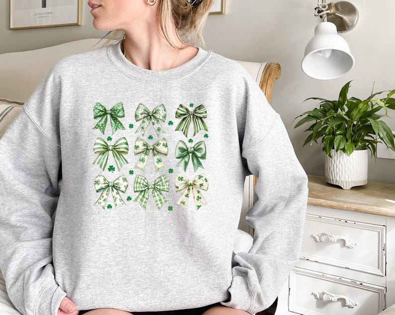 May include: A gray sweatshirt with a pattern of green and white shamrock bows. The bows are arranged in a grid pattern on the front of the sweatshirt.