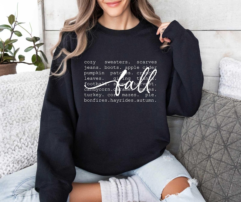 Pu&ograve; includere: Felpa nera con testo bianco che recita "cozy sweaters, scarves, jeans, boots, apple cider, pumpkin patches, crisp leaves, giving thanks, fall, football, s'mores, harvest, candy corn, caramel apples, turkey, corn mazes, pie, bonfires, hayrides, autumn."