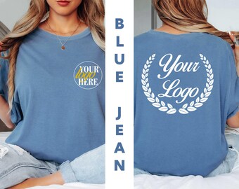 May include: A blue jean colored t-shirt featuring a small circular logo on the front left chest that reads YOUR LOGO HERE in yellow and white text. The back of the shirt displays a large white laurel wreath graphic with the text Your Logo.