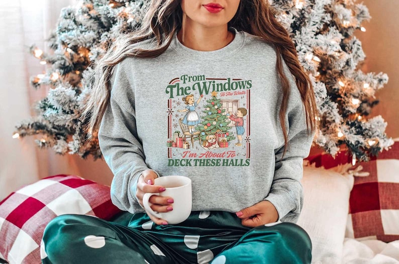 May include: A gray sweatshirt with a festive Christmas graphic. The graphic features a decorated Christmas tree, a woman, a child, and the text "From The Windows To All The Walls I'm About To Deck These Halls."