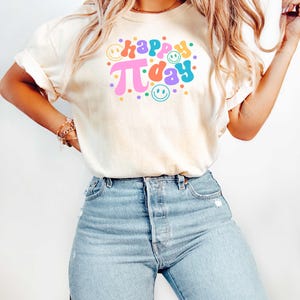 May include: A white t-shirt with the text "happy pi day" in colourful retro font with smiley faces and colourful dots.