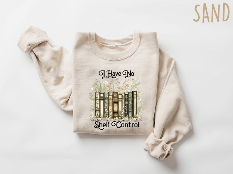 May include: A sand-colored sweatshirt with the text "I Have No Shelf Control" in black script. The graphic features a row of books with floral accents. The sweatshirt is made of a soft material.