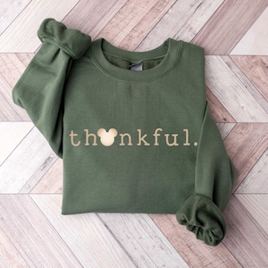 May include: A green sweatshirt with a gold Mickey Mouse head and the word "thankful" printed on the front.