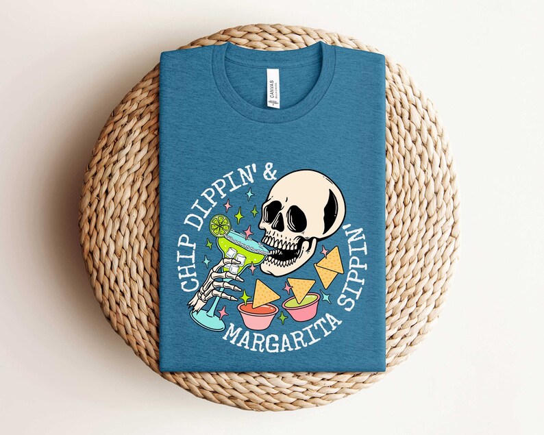 Pu&ograve; includere: Una maglietta blu con una grafica bianca di uno scheletro che beve una margarita e il testo "Chip Dippin' & Sippin' Margarita".