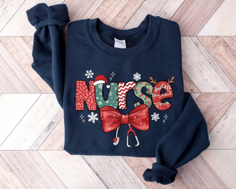 May include: Navy blue sweatshirt with a Christmas-themed design featuring the word "NURSE" in colorful, patterned letters with a red bow and a stethoscope.