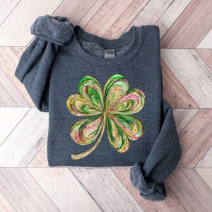 May include: A dark gray sweatshirt with a green, gold, and pink four-leaf clover design.