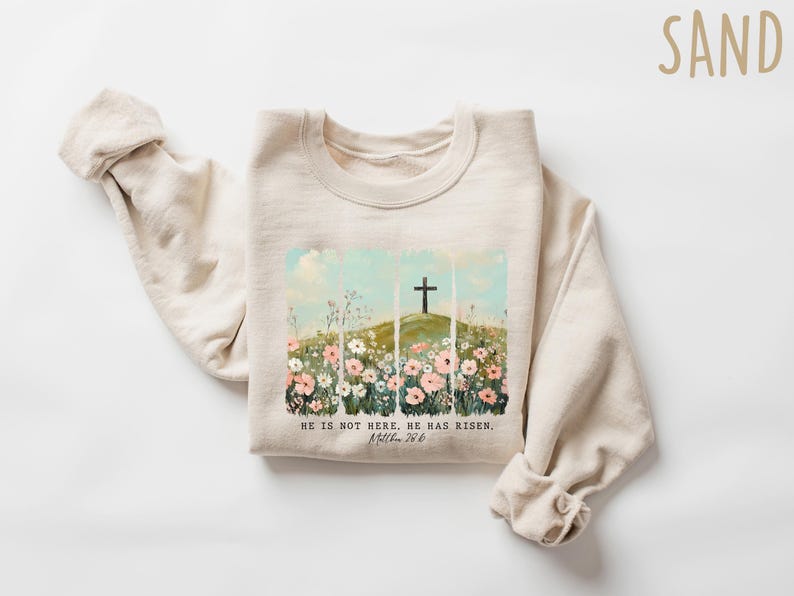 May include: A beige sweatshirt with a graphic print of a cross on a hill with flowers. The text "He is not here. He has risen. Matthew 28:6" is printed below the graphic.