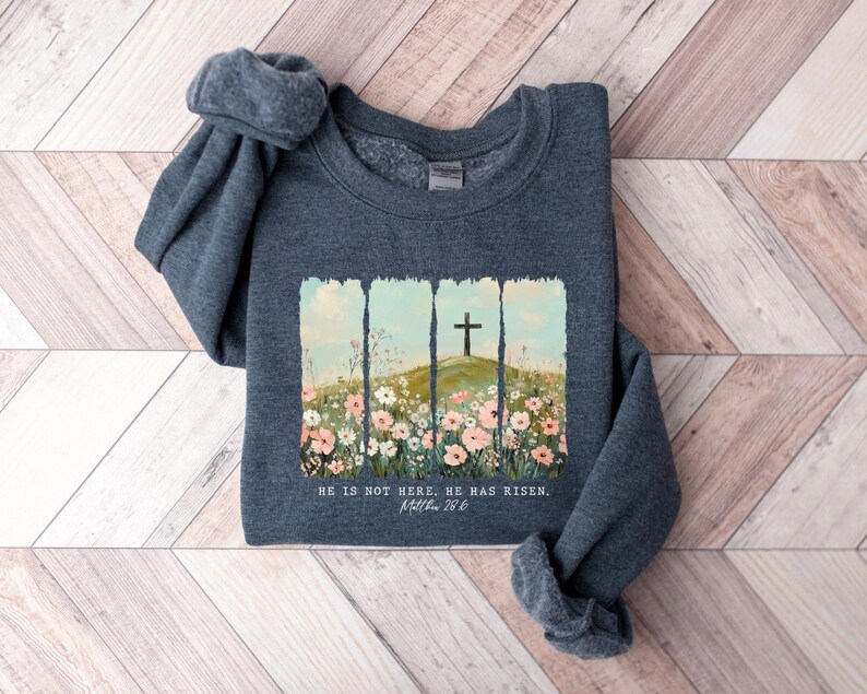 May include: A dark gray sweatshirt with a floral design and a cross on a hill. The text "He is not here. He has risen.  Matt. 28:6" is printed on the sweatshirt.