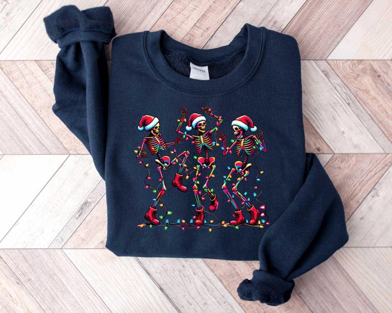 May include: A navy blue sweatshirt with a Christmas-themed design featuring three skeletons wearing Santa hats and dancing with colorful lights.