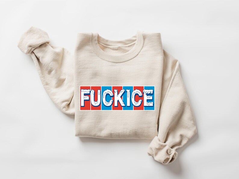 以下が含まれることがあります： 赤、白、青のデザインで「FUCKICE」の文字がプリントされたベージュ色のスウェットシャツ。スウェットシャツは折りたたまれ、袖は丸められています。グラフィックは言葉遊びです。