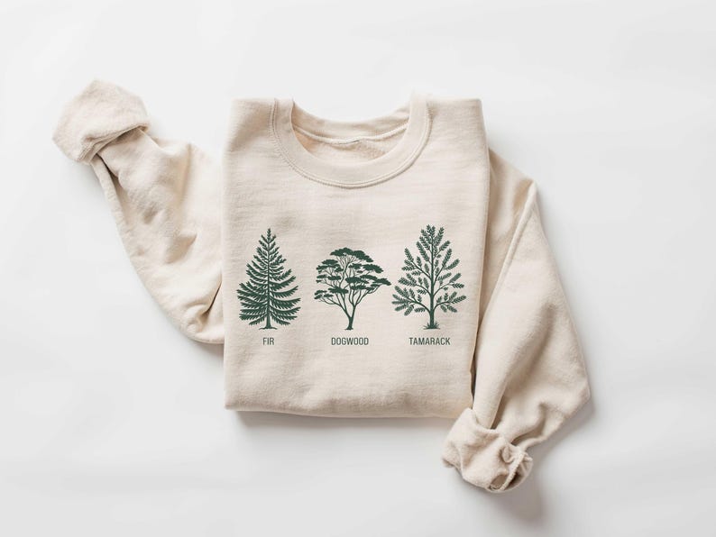 Pu&ograve; includere: Una felpa beige con una grafica di tre alberi, etichettati "Fir", "Dogwood" e "Tamarack".