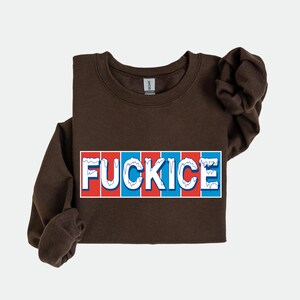 以下が含まれることがあります： 赤、白、青のブロックレターデザインで「FUCKICE」という文字が入った茶色のスウェットシャツ。スウェットシャツは長袖で、クルーネックです。
