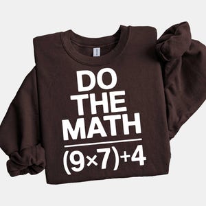 May include: A dark brown sweatshirt with the phrase "DO THE MATH" in large white block letters. Below the text is the equation (9x7)+4 in white. The sweatshirt has a crew neck and long sleeves.