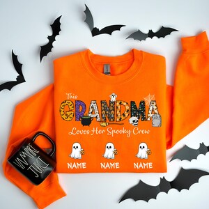 May include: Orange Halloween sweatshirt with the text "This Grandma Loves Her Spooky Crew". The word "GRANDMA" is decorated with Halloween-themed patterns. Below are three ghost graphics holding pumpkins, with space for names.