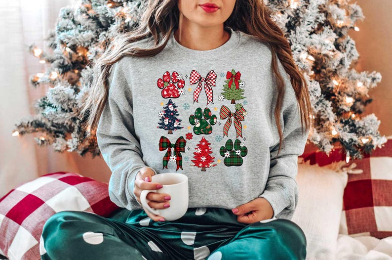 May include: A gray sweatshirt with a Christmas-themed design featuring paw prints, bows, and Christmas trees. The design is in red, green, and white.
