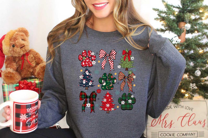 May include: A gray sweatshirt with a Christmas-themed design featuring paw prints, bows, and Christmas trees. The design is in red, green, and white.