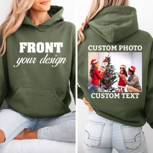 May include: An olive green hooded sweatshirt featuring a front graphic with the text FRONT your design. The back displays a custom photo of two people in Santa hats decorating a Christmas tree, with the text CUSTOM PHOTO and CUSTOM TEXT.