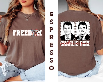May include: Espresso-colored t-shirt with the word "FREEDOM" in white block letters and a red, white, and blue bow graphic. The back of the shirt features two portraits of a man and the text "CHARLIE KIRK".