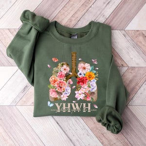 May include: A green sweatshirt with a floral design of lungs and the text "YHW", which stands for "every breath you take, breathe life into the home".