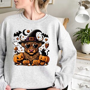 May include: A gray sweatshirt with a Halloween-themed design featuring a Highland cow wearing a witch's hat and sunglasses, surrounded by pumpkins, bats, and candy.