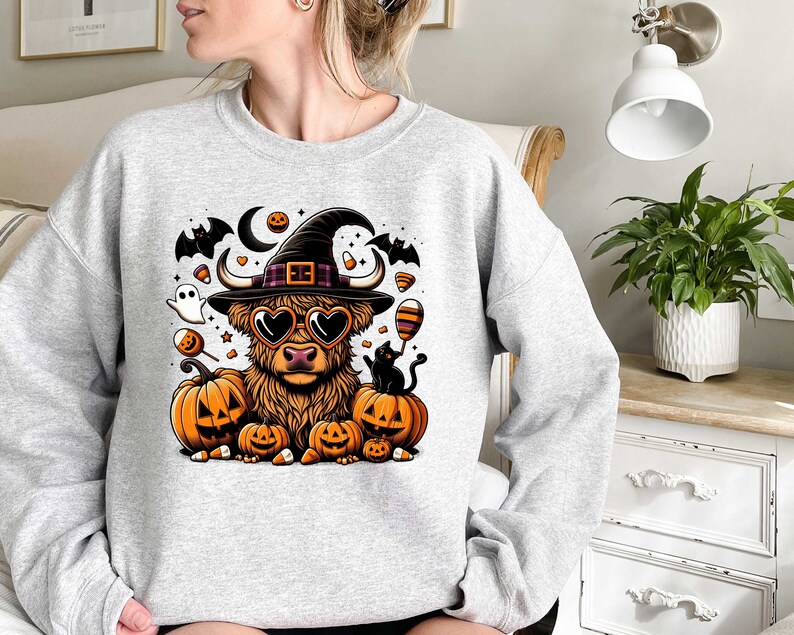 May include: A gray sweatshirt with a Halloween-themed design featuring a Highland cow wearing a witch's hat and sunglasses, surrounded by pumpkins, bats, and candy.
