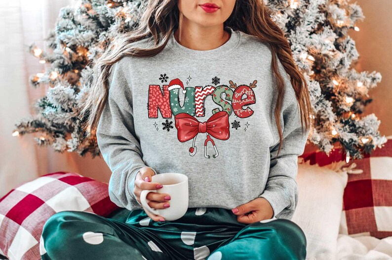 May include: A gray sweatshirt with a Christmas-themed design that says "Nurse" in colorful letters with a red bow and a stethoscope.