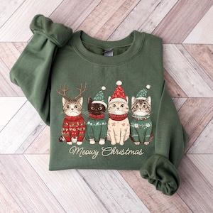 May include: Green sweatshirt with a Christmas-themed design featuring four cats wearing Santa hats and sweaters. The text "Meowy Christmas" is printed below the cats.