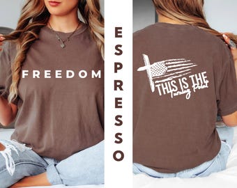 May include: Espresso-colored t-shirt with the word "FREEDOM" in white block letters on the front. The back features a white cross with an American flag design and the text "THIS IS THE Turning Point".