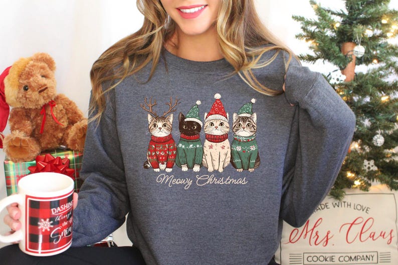 May include: A gray sweatshirt with a Christmas-themed design featuring four cats wearing Santa hats and sweaters. The text "Meowy Christmas" is printed below the cats.