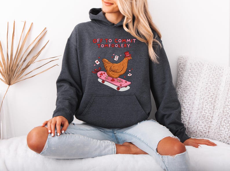 K&ouml;nnte beinhalten: Dunkelgrauer Kapuzenpullover mit einem Aufdruck eines Huhns auf einem Skateboard. Das Huhn tr&auml;gt einen Hut, das Skateboard ist rosa mit Herzen. Der Text "OFF TO COMMIT TOMFOOLERY" steht dar&uuml;ber.