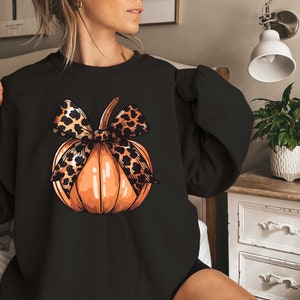 May include: Black sweatshirt with a graphic of an orange pumpkin with a leopard print bow.