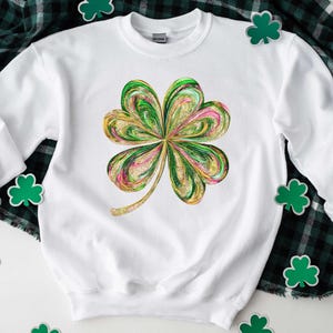 May include: White sweatshirt with a green, gold, and pink four-leaf clover design. The clover is stylized with a swirling, marbled pattern.