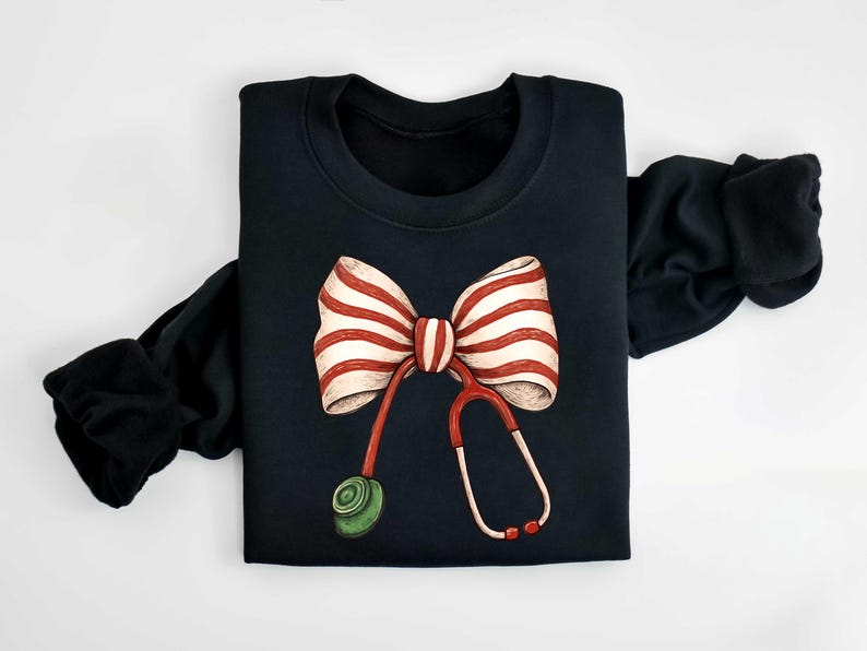 May include: Black sweatshirt featuring a whimsical design of a red and white striped bow and a stethoscope. The stethoscope has red tubing and a green earpiece. The sleeves are black.