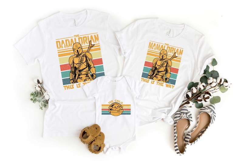 May include: White t-shirts with a retro design featuring a Mandalorian character and the text "The Dadalorian", "The Mamalorian", and "The Child". The shirts have the text "This is the way" printed on them.