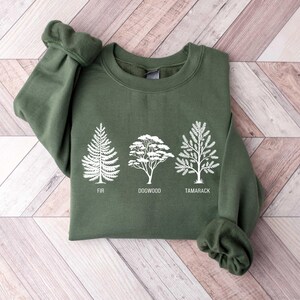 Pu&ograve; includere: Una felpa verde con una grafica bianca di tre alberi. Gli alberi sono etichettati "Fir", "Dogwood" e "Tamarack".