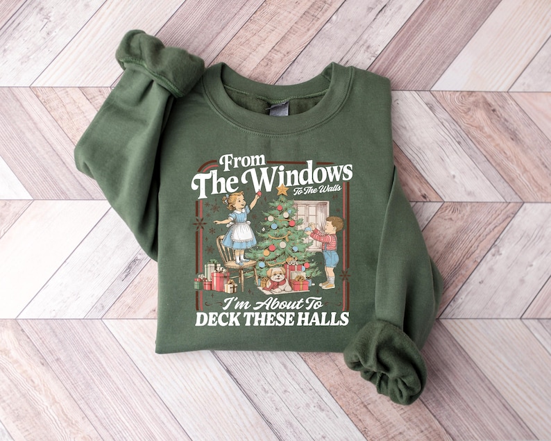 May include: Green sweatshirt with a Christmas-themed graphic. The graphic features a vintage illustration of children decorating a Christmas tree, with the text "From The Windows To The Walls, I'm About To Deck These Halls."