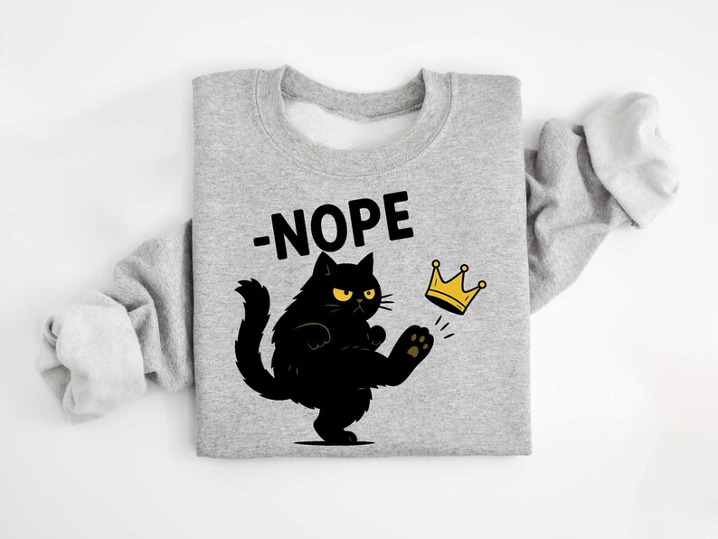 May include: A grey sweatshirt featuring a black cat kicking a gold crown. The word "-NOPE" is above the cat. The cat has yellow eyes and is kicking the crown with its paw.