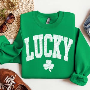 Peut inclure: Sweat-shirt vert avec un graphisme blanc de style vintage qui dit "LUCKY" avec un tr&egrave;fle &agrave; quatre feuilles en dessous.