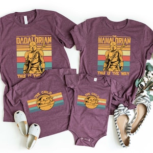 May include: A set of four maroon t-shirts with a retro-style graphic of a Mandalorian character. The shirts feature the text "The Dadalorian", "The Mamalorian", and "The Child".