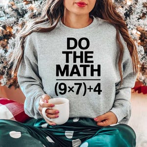 May include: A light gray sweatshirt with the text "DO THE MATH" above the equation (9x7)+4. The person is holding a white mug. The person is wearing green satin pants with white polka dots. A Christmas tree is in the background.