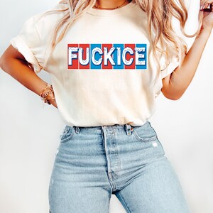 以下が含まれることがあります： 「FUCKICE」の文字が赤、白、青の長方形のデザインでプリントされたクリーム色のTシャツ。明るいブルーデニムのジーンズと合わせています。
