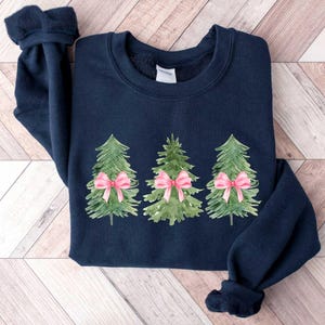 May include: A navy blue sweatshirt with a design of three green watercolor Christmas trees with pink bows.