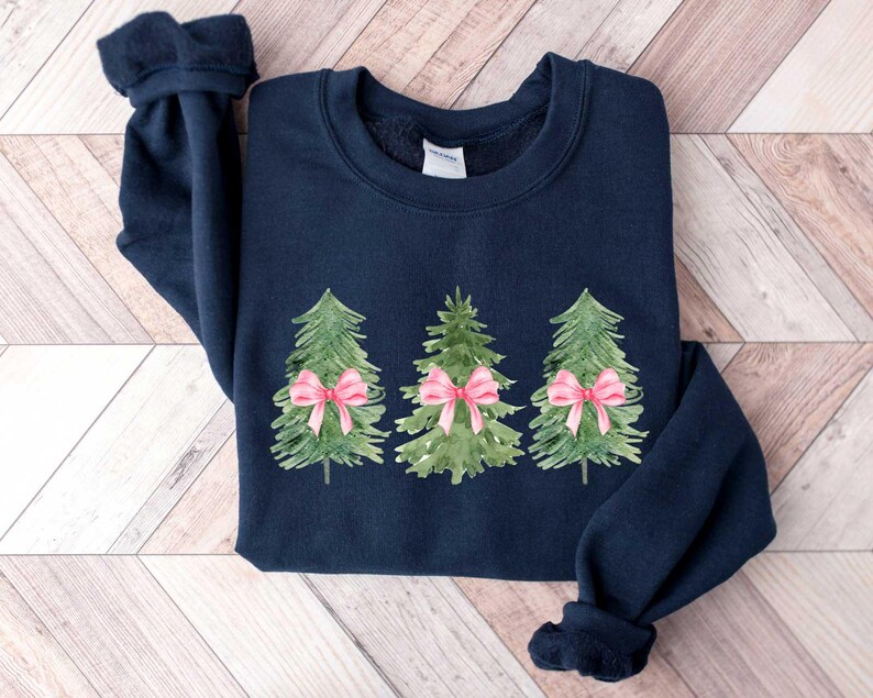 May include: A navy blue sweatshirt with a design of three green watercolor Christmas trees with pink bows.