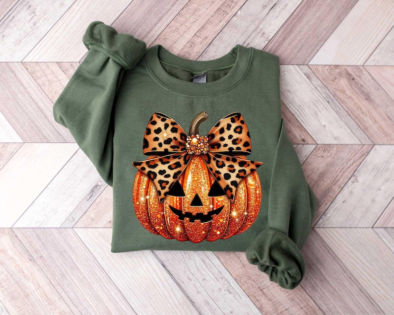 Peut inclure: Sweat-shirt vert avec un motif de citrouille sculpt&eacute;e. La citrouille est orange avec des paillettes et un n&oelig;ud en imprim&eacute; l&eacute;opard noir et marron sur le dessus.