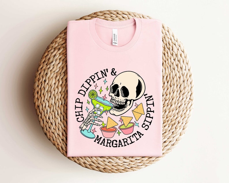 Pu&ograve; includere: Maglietta rosa con una grafica di uno scheletro che beve una margarita e il testo "Chip Dippin' & Sippin' Margarita".