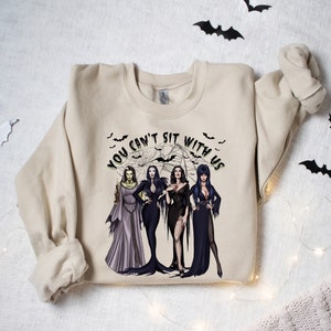 May include: A beige sweatshirt with a graphic print of four women in black dresses and the text "You can't sit with us".