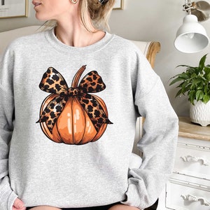 May include: A gray sweatshirt with a graphic of an orange pumpkin with a leopard print bow.