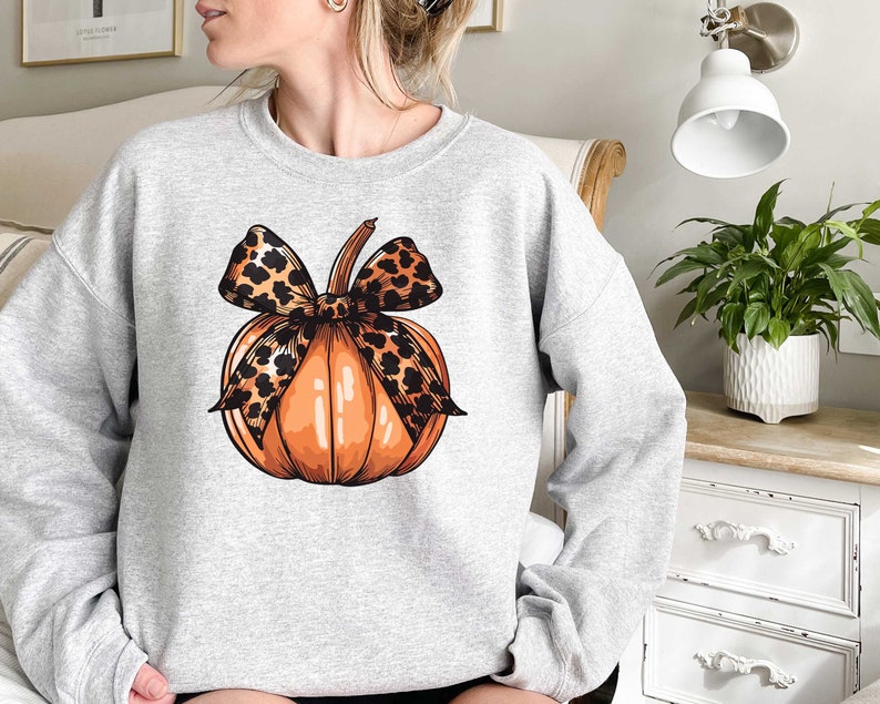 May include: A gray sweatshirt with a graphic of an orange pumpkin with a leopard print bow.