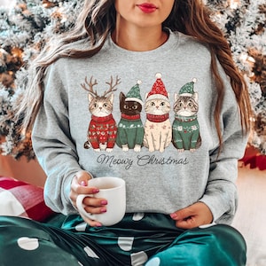 May include: A gray sweatshirt with a Christmas-themed design featuring four cats wearing Santa hats and sweaters. The text "Meowy Christmas" is printed below the cats.