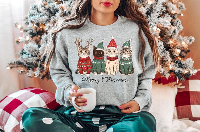 May include: A gray sweatshirt with a Christmas-themed design featuring four cats wearing Santa hats and sweaters. The text "Meowy Christmas" is printed below the cats.